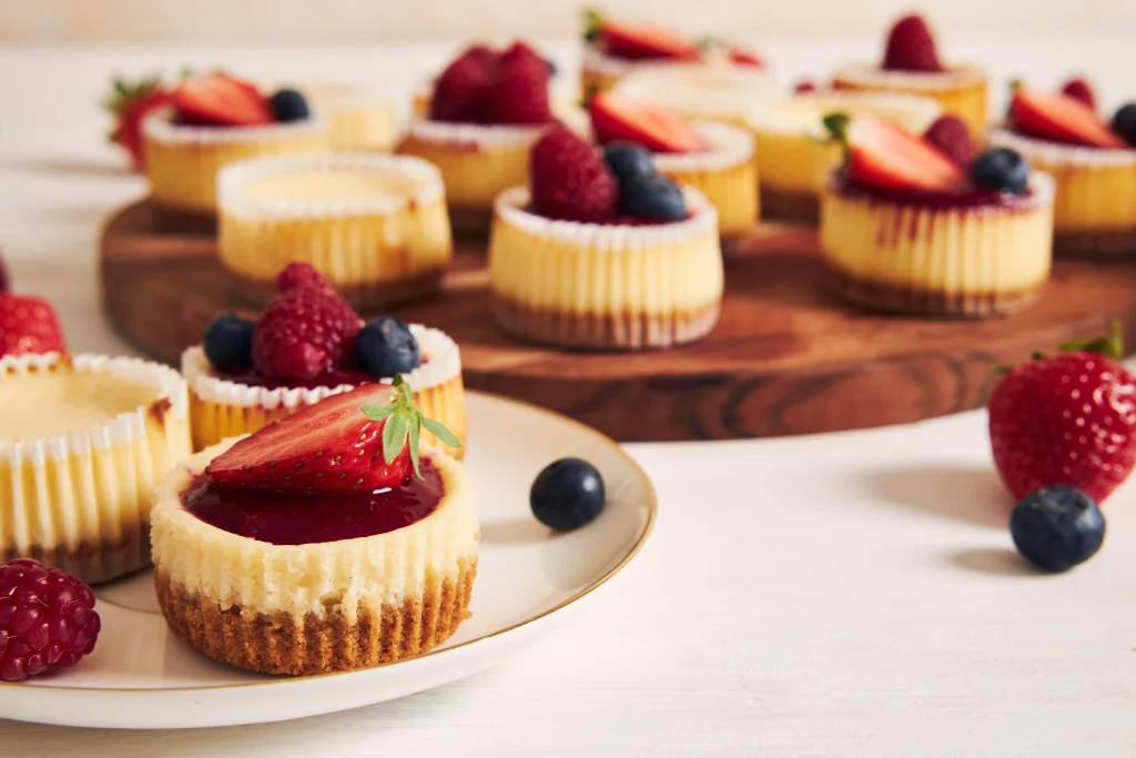 Mini cheesecake cupcakes topped with strawberries, blueberries, and raspberry sauce