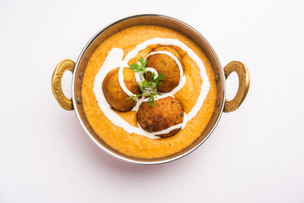 Malai kofta curry with fried paneer and potato balls in creamy gravy topped with fresh cream and coriander