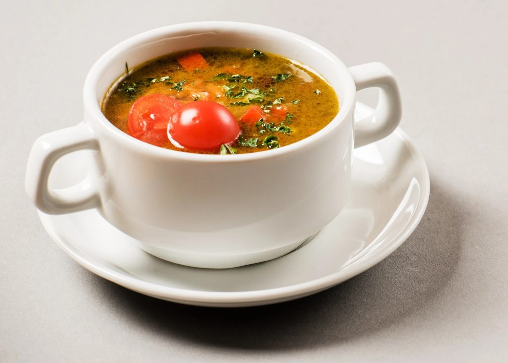 Tomato Rasam served in a white soup bowl with fresh cherry tomatoes and coriander garnish