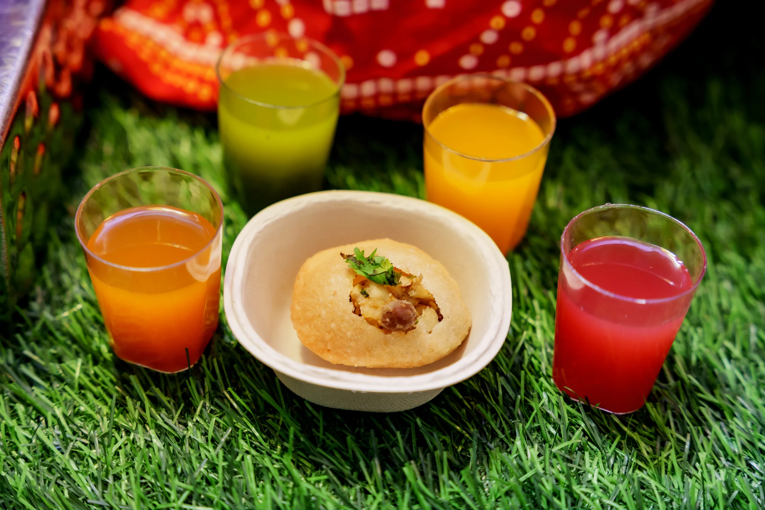 A serving of Pani Puri accompanied by colorful drinks on a grass-like surface, perfect by a Sar V Sri North Indian catering services