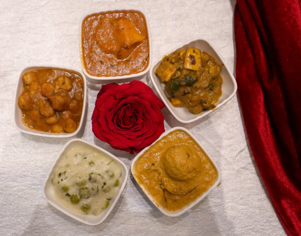 A variety of North Indian curries including chickpea curry, paneer curry, and vegetable curry, served in small bowls with a rose garnish