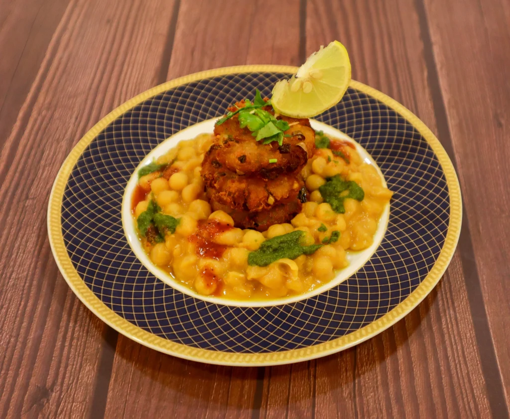 Aloo tikki served with chickpea curry, garnished with fresh cilantro and a slice of lime, on a decorative plate by SarVSri Caterers