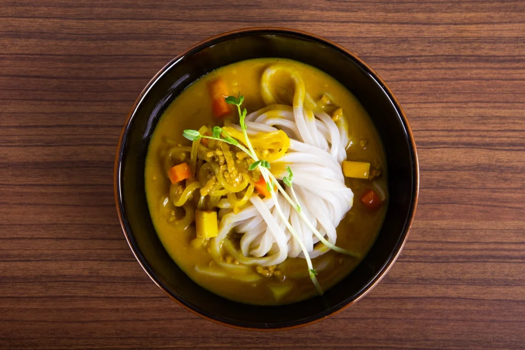 Burmese noodle soup with vegetables in a flavorful curry broth, garnished with fresh herbs, served in a black bowl