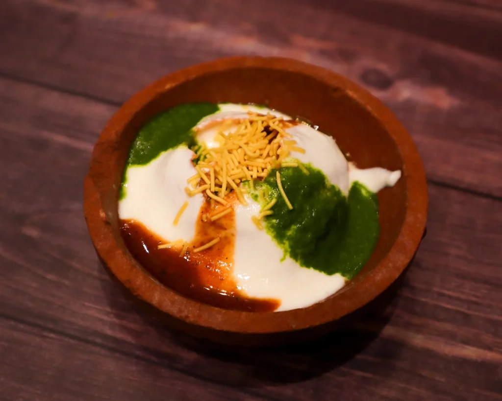 Delicious Dahi Puri served in a traditional clay bowl with yogurt, green chutney, tamarind sauce, and crispy sev garnish