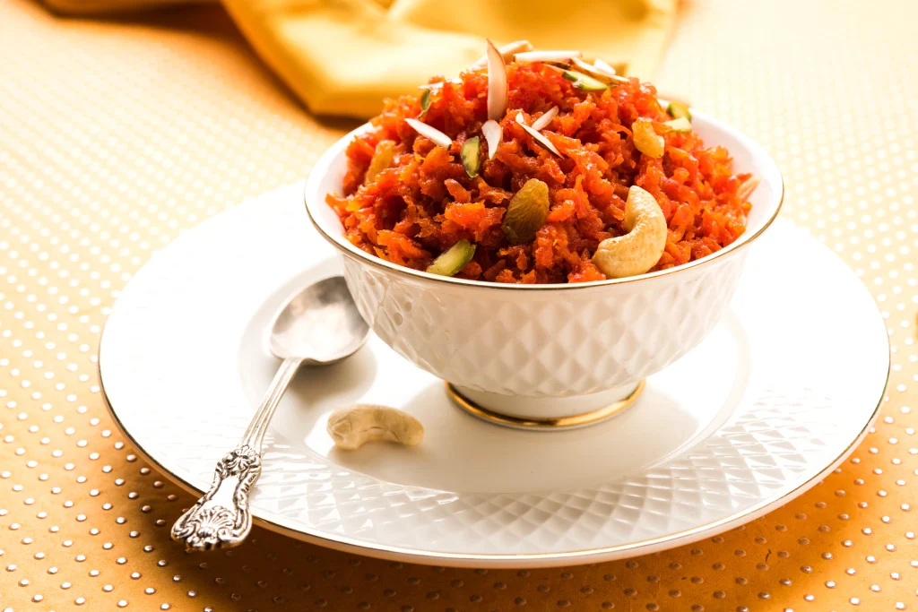 Gajar Halwa (Carrot Halwa) garnished with cashews, almonds, and pistachios in a white bowl, served by a Sar V Sri Jain Catering Services