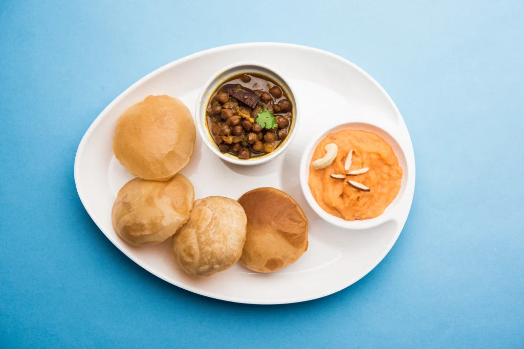 Jain Poori served with Chole (spicy chickpea curry) and sweet halwa, garnished with nuts