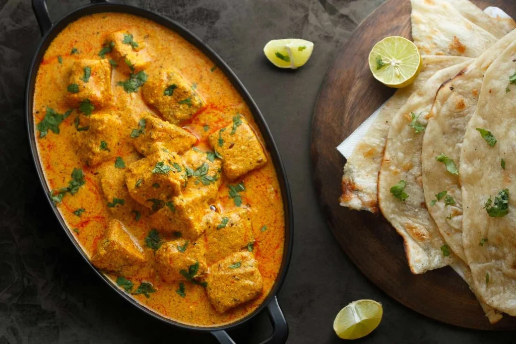 Paneer Butter Masala served with naan and garnished with cilantro