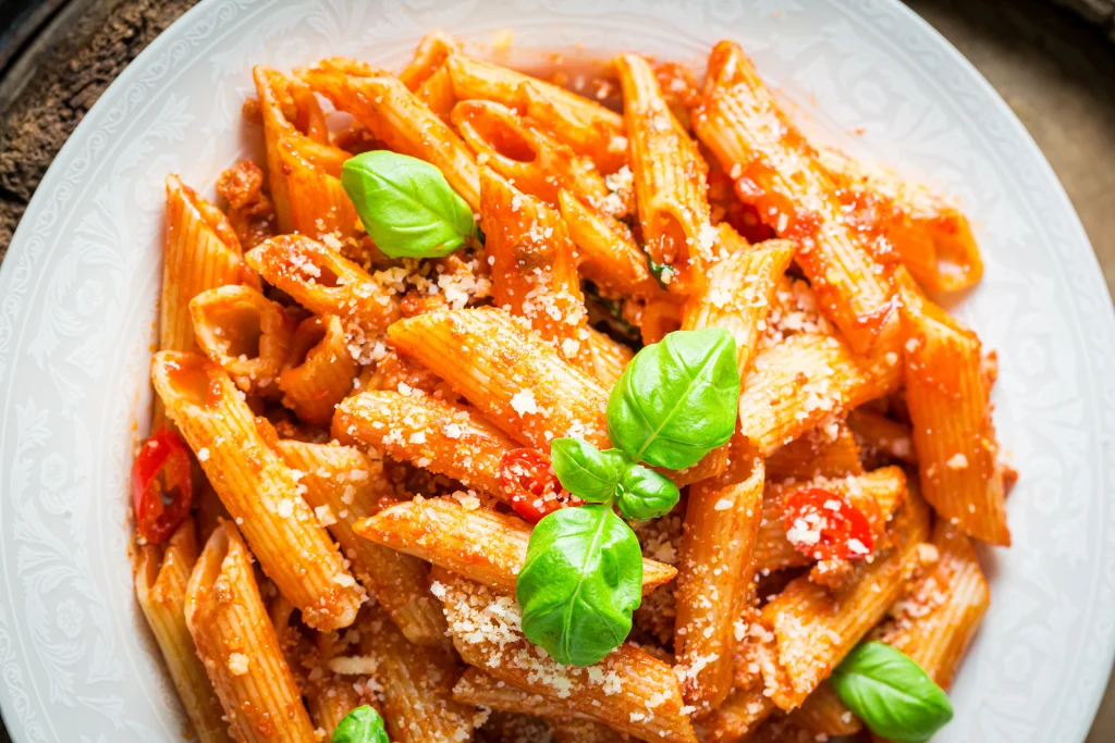 Plate of penne arrabbiata pasta with fresh basil leaves, grated parmesan cheese, and a flavorful tomato sauce