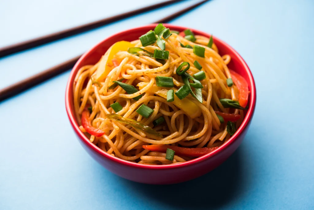 Szechuan Chinese noodles with colorful bell peppers and spring onions on a plate by Sar V Sri Chinese catering services