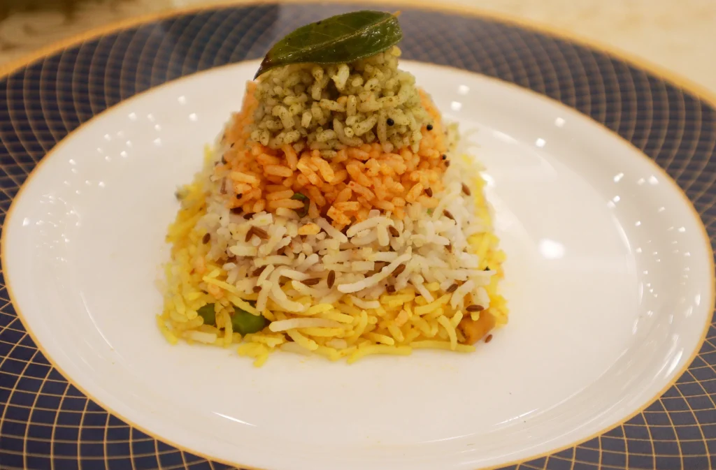 Jain-friendly rice dish with layers of colorful rice, garnished with a curry leaf, served on a white plate