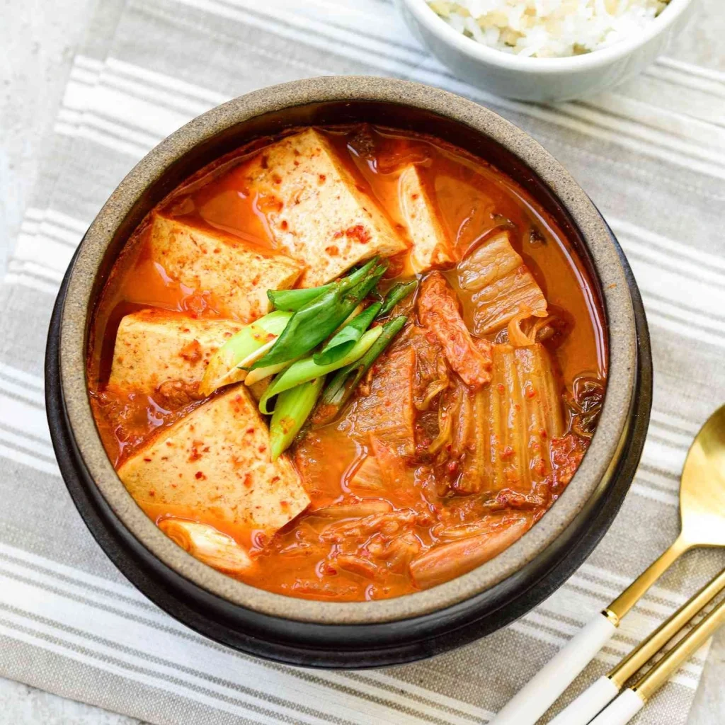 Korean Kimchi Jjigae (Kimchi Stew) with tofu, kimchi, and green onions in a traditional stone pot, served by Sar V Sri korean catering services