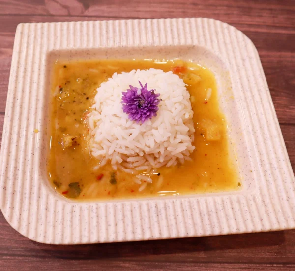 South Indian rice dish served with dal sambar, garnished with a purple flower, on a square plate